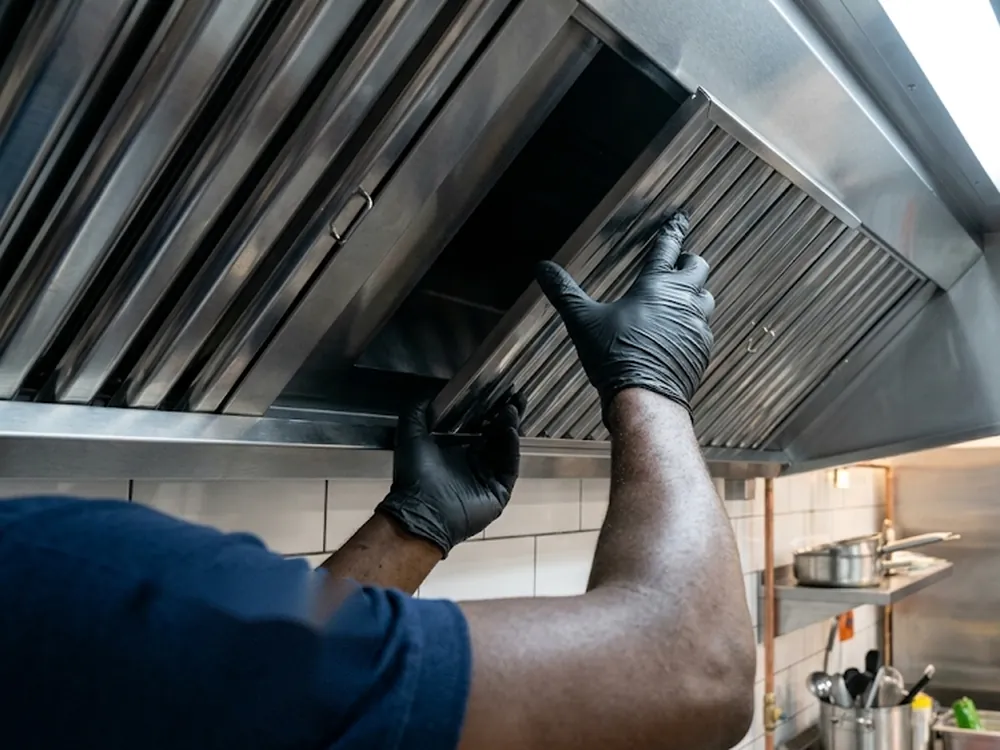 Technicien mettant en place un filtre à graisse dans une hotte professionnelle de cuisine