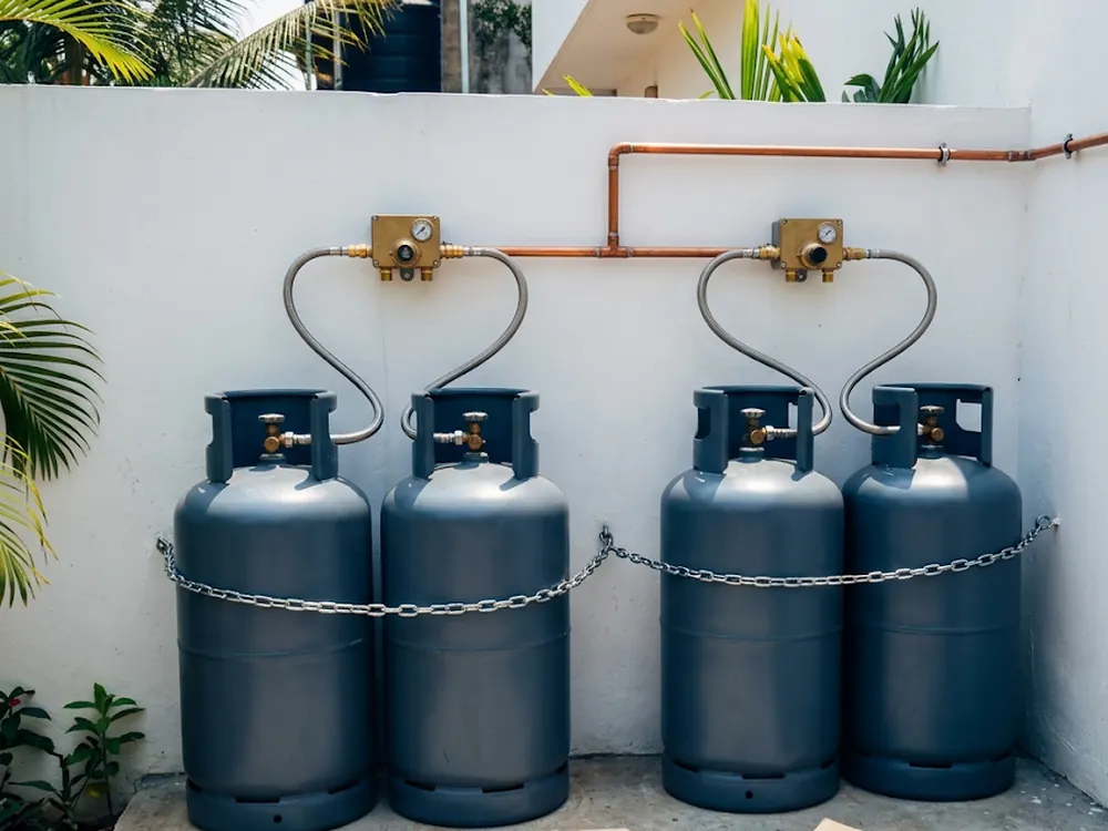 Centrale de quatre bouteilles de gaz reliées par des flexibles inox à deux détendeurs et à une conduite en cuivre, installée à l'air libre